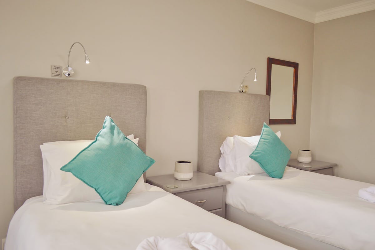 A hotel room with two beds, each with a pillow and a bedside table with a lamp.