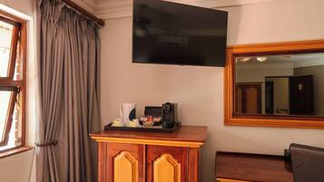 A hotel room with a flat-screen TV mounted on the wall, a wooden cabinet with a tray of coffee-making items, and a large mirror.