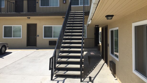 A multi-story building with a central staircase, exterior windows, and a vehicle parked in front. - Ace Budget Motel (San Diego)