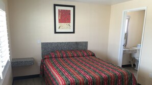 A bedroom with a bed, a framed picture on the wall, a small shelf, and a bathroom visible through an open door. - Ace Budget Motel (San Diego)