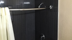 A bathroom with dark tiled walls, a metal towel rack, and a shower area. - Ace Budget Motel (San Diego)