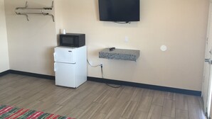A compact kitchenette with a microwave, mini-fridge, and a TV mounted on the wall. - Ace Budget Motel (San Diego)