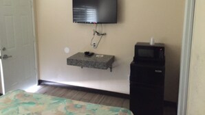 A room with a bed, a television mounted on the wall, a small shelf, and a microwave. - Ace Budget Motel (San Diego)