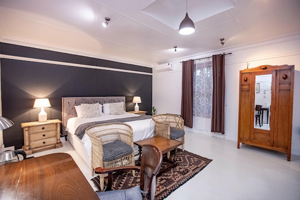 Habitación de hotel con cama, dos sillones de mimbre, una mesa de madera, armario y espejo.