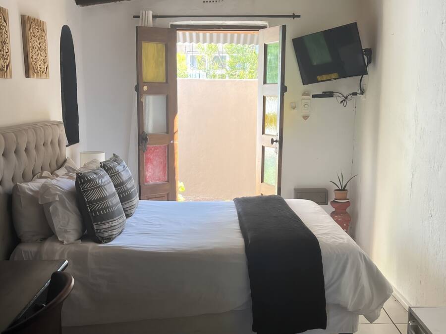 Un dormitorio con cama, televisor montado en la pared, ventilador de techo y ventana con vista a follaje.