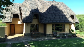 A two-story house with a steeply pitched roof, stone foundation, and a front porch with a bench. - Champagne Haven (Cathkin Park)