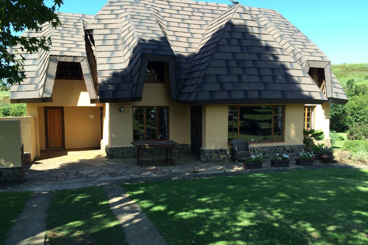 A two-story house with a steeply pitched roof, stone foundation, and a front porch with a bench.