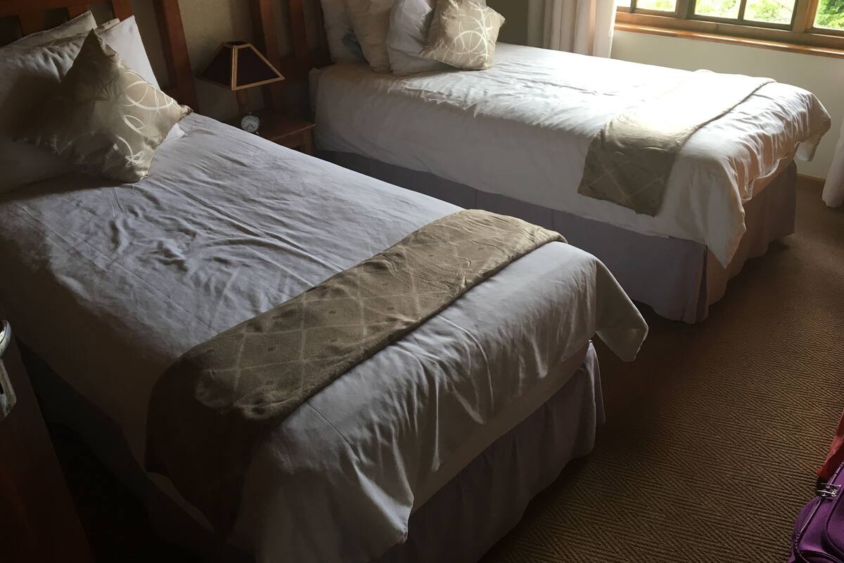 A room with two beds, a wooden headboard, a nightstand with a lamp, and a window with curtains.