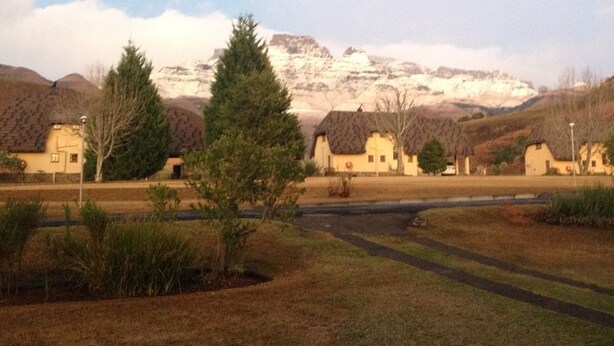 A rural landscape with traditional houses, a car, and a mountain in the background. - Champagne Haven (Cathkin Park)