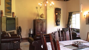 A traditional room with a wooden ceiling, a chandelier, a wooden cabinet, and a dining table set with a placemat and a centerpiece. - Champagne Haven (Cathkin Park)