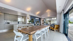 A modern kitchen with a central island, white chairs, and a wooden table. - Le Paradis Penthouse Apartment (Hermanus)