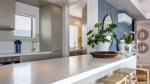 A modern kitchen with a large island, wooden stools, and a potted plant. - Le Paradis Penthouse Apartment (Hermanus)