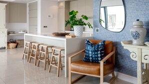 A modern kitchen with a central island, bar stools, a potted plant, and a decorative mirror. - Le Paradis Penthouse Apartment (Hermanus)