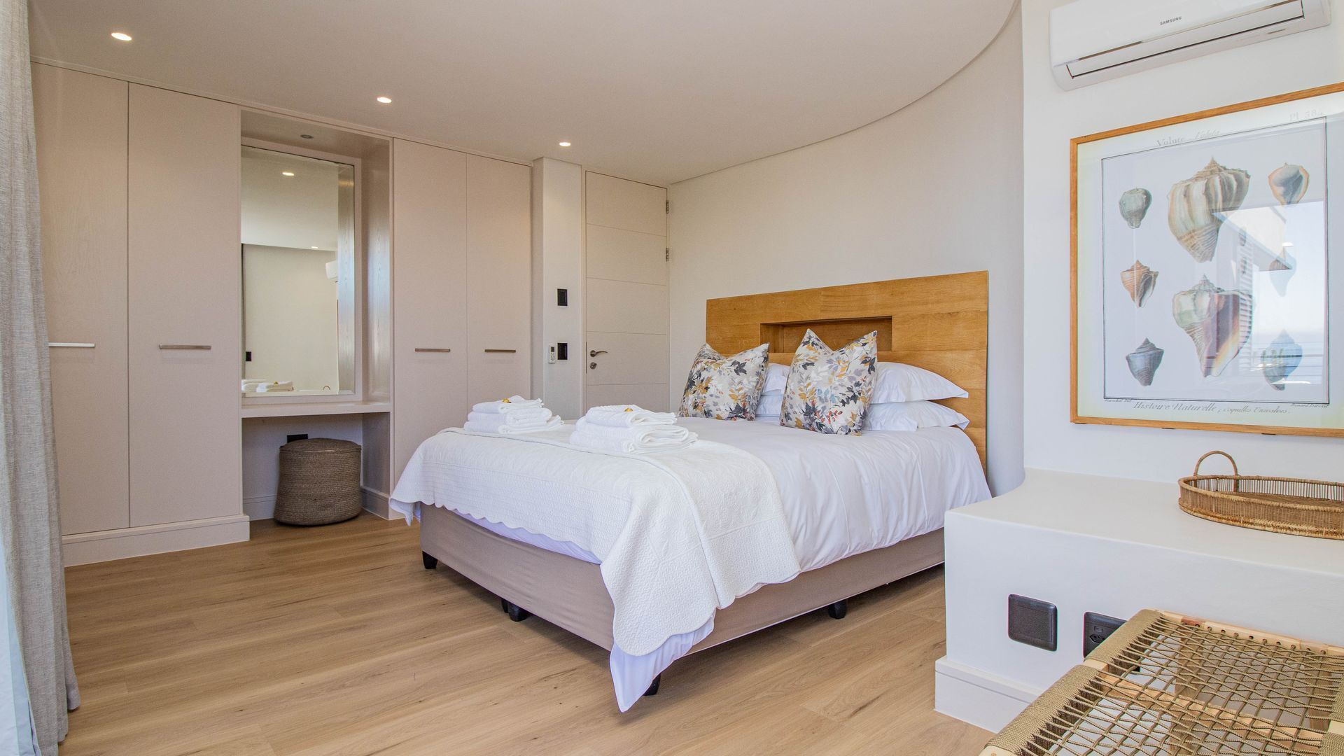 A bedroom with a bed, a wooden headboard, a large mirror, a wardrobe, and a framed picture on the wall.