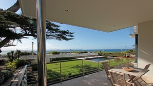 Un balcon avec vue sur la mer, une piscine et un coin repas avec des chaises et une table.