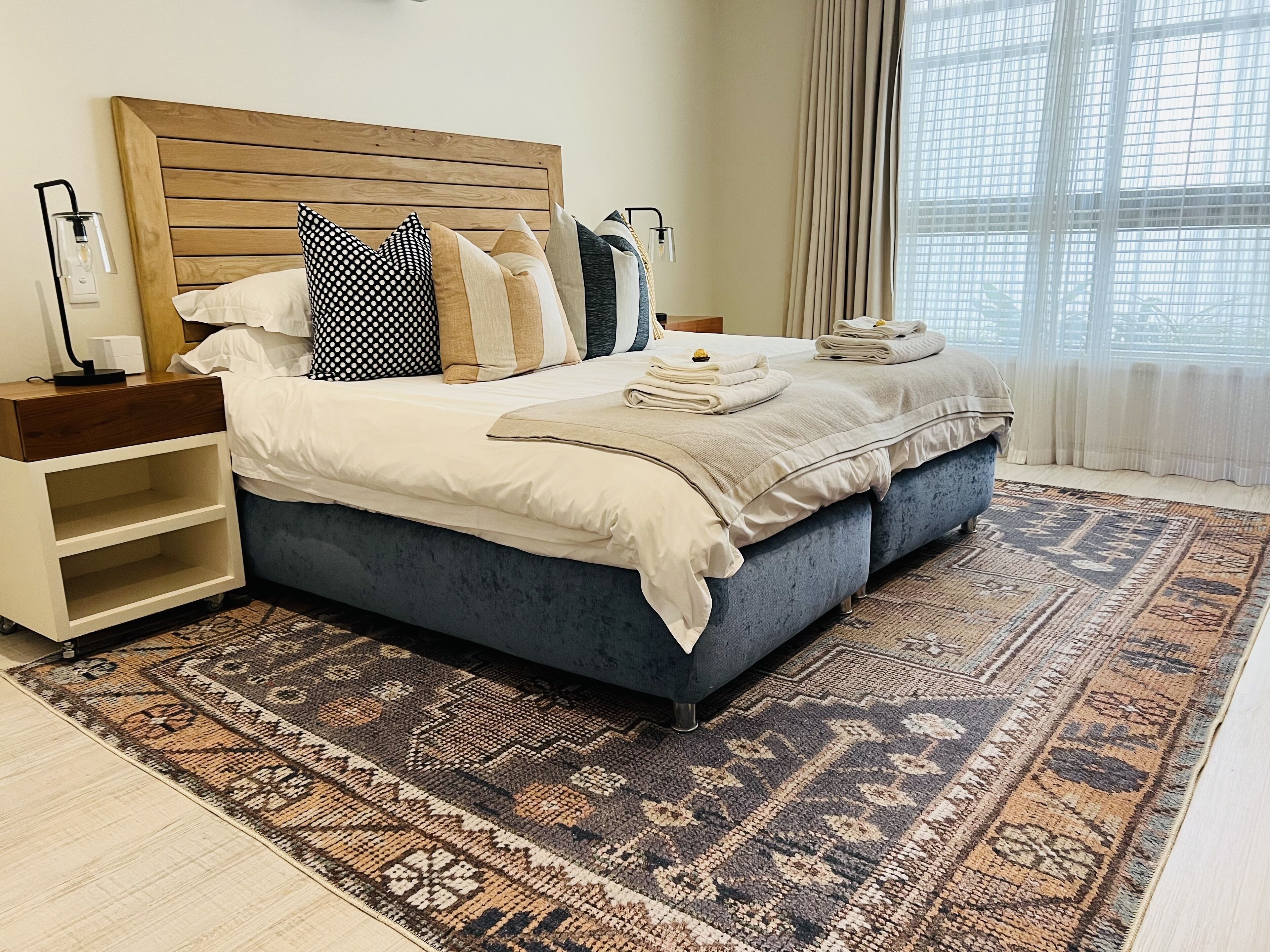 A double bed with a wooden headboard, a patterned rug, and a bedside table with a lamp.