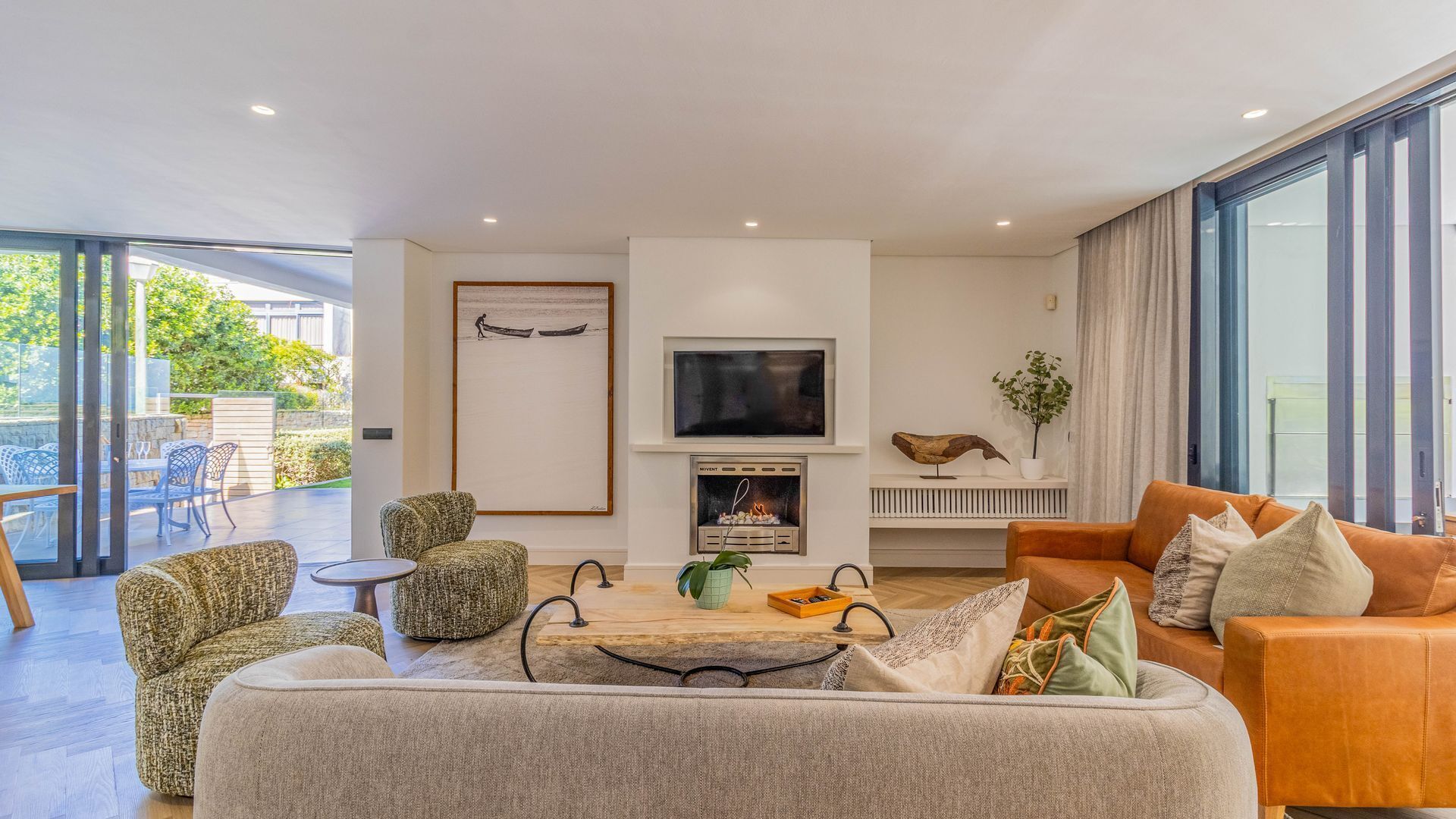 A modern living room with a fireplace, comfortable seating, a television, and a view of the outdoors.
