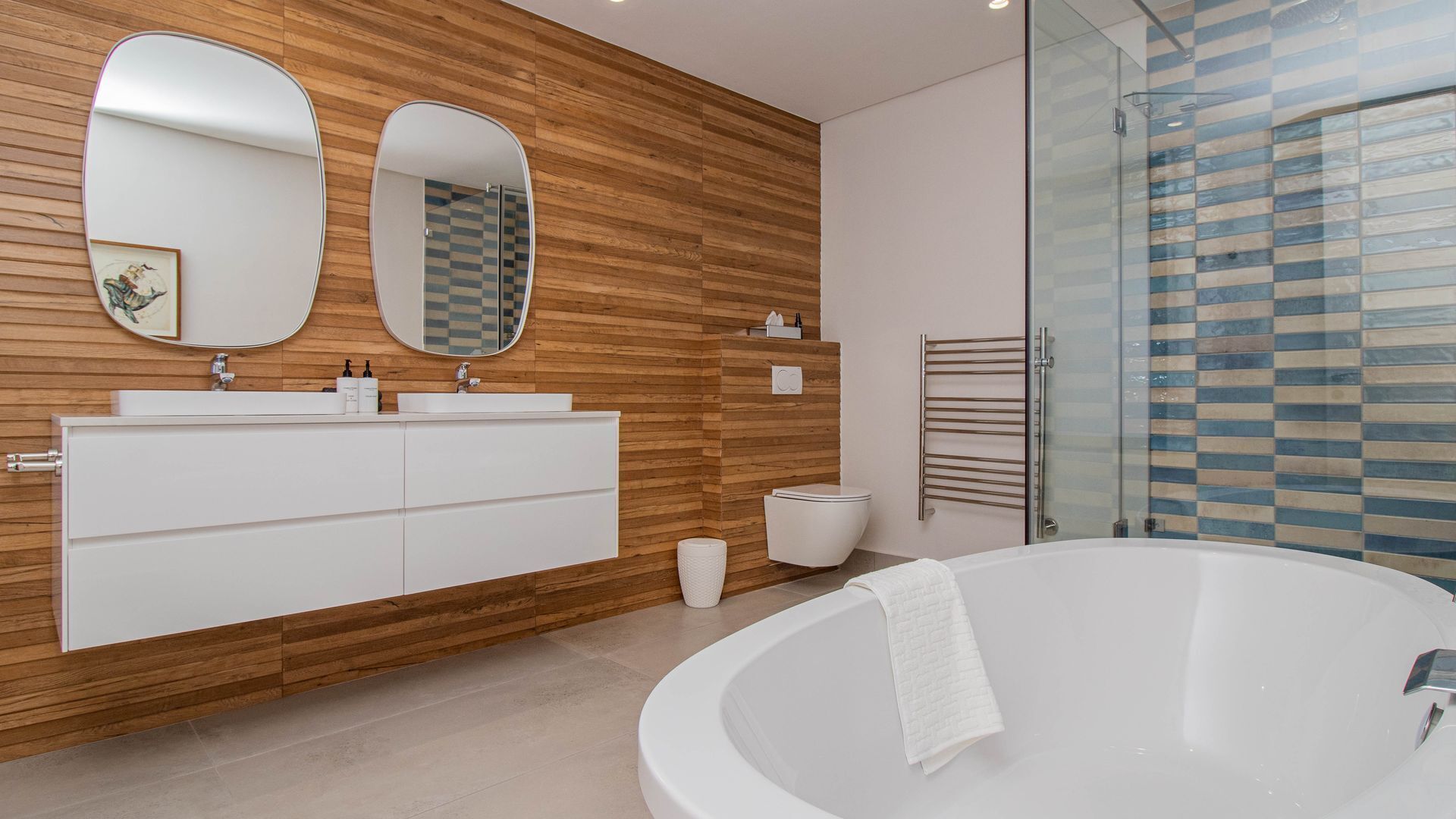 A modern bathroom with a wooden vanity, two mirrors, a white bathtub, and a glass shower enclosure.