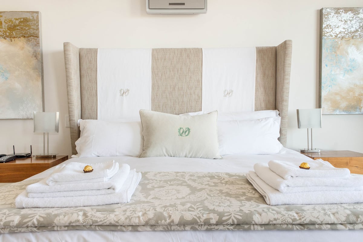 A neatly made bed with folded towels and a decorative pillow, a bedside table with a lamp, and artwork on the walls.