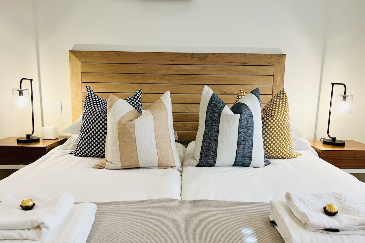 A neatly made bed with multiple pillows, two bedside tables with lamps, and a wooden headboard.