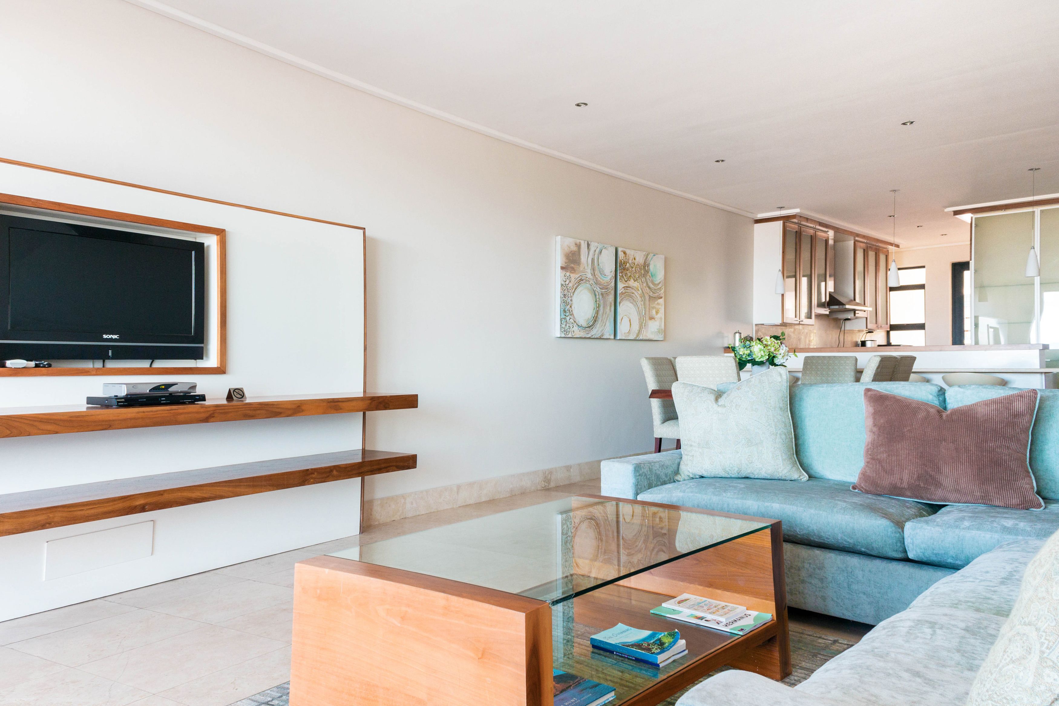 A modern living room with a glass coffee table, a sofa, and a flat-screen TV mounted on the wall.