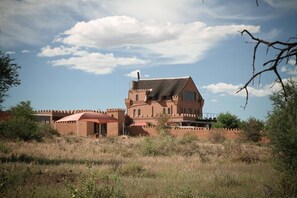 A large, castle-like building with a prominent tower and arched windows, surrounded by a dry, grassy landscape. - Sweet Thorn Retreat Airport Lodge (Windhoek)