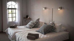 Un lit double avec des coussins à motifs, une table de chevet avec une lampe et une fenêtre avec des rideaux.