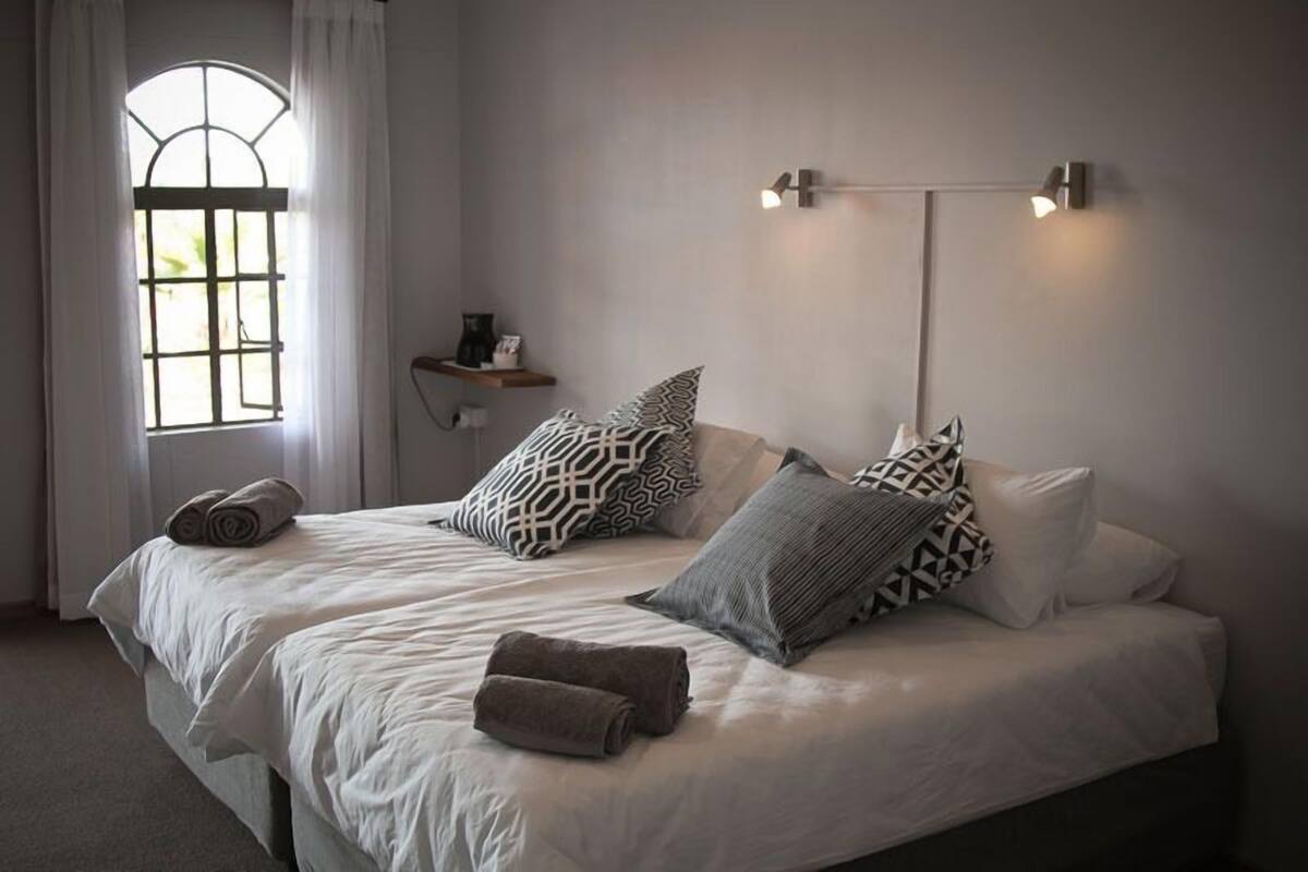 Ein Doppelbett mit gemusterten Kissen, ein Nachttisch mit Lampe und ein Fenster mit Vorhängen.