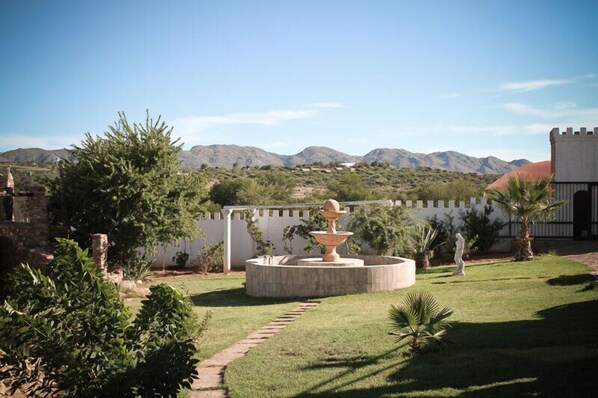 A courtyard with a fountain, a statue, and a view of mountains. - Sweet Thorn Retreat Airport Lodge (Windhoek)