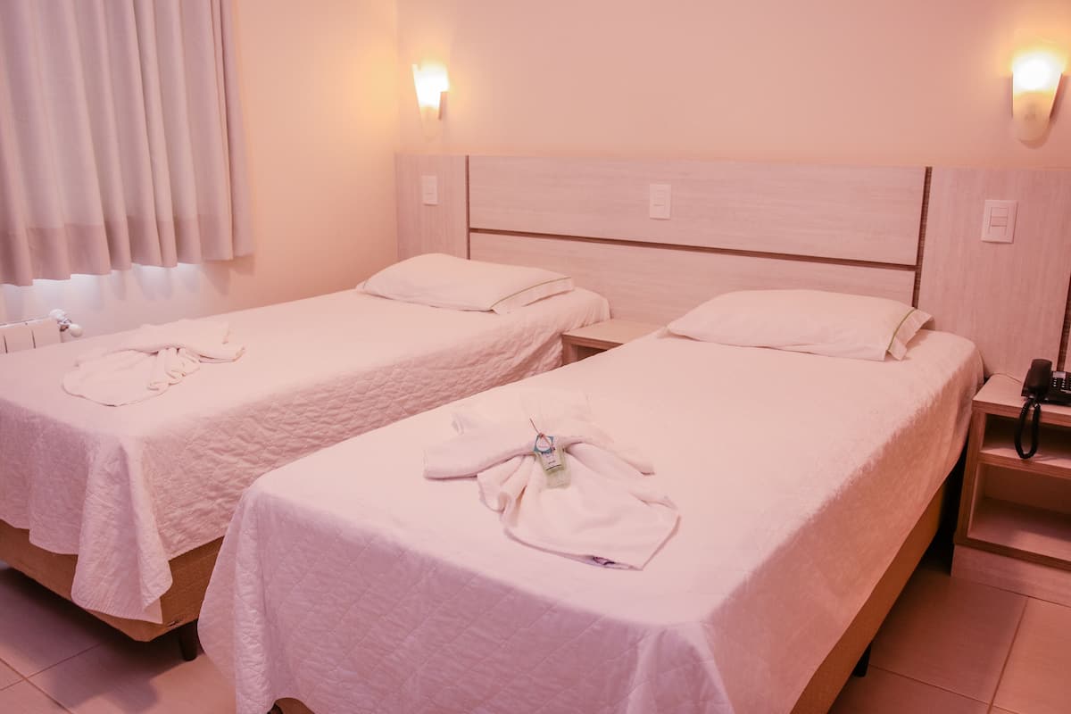 Ett hotellrum med två sängar, där varje säng har en prydligt vikt handduk och en telefon vid sängbordet.