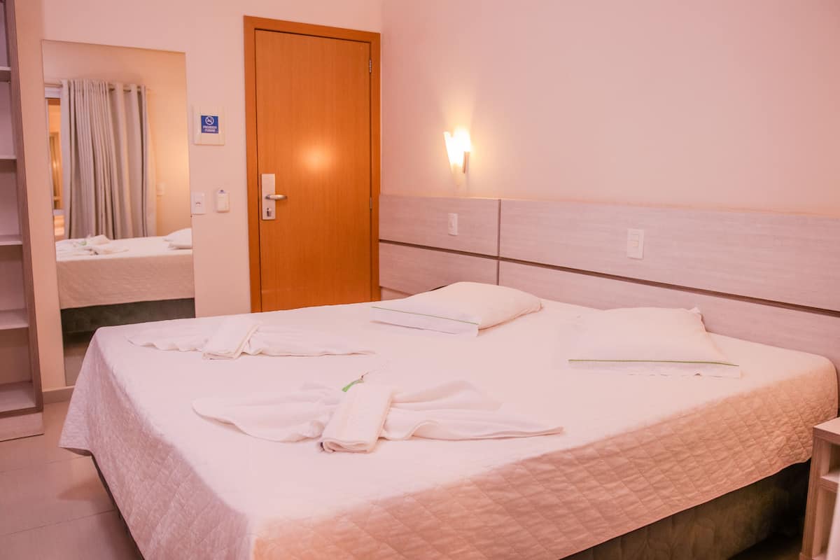 Ett hotellrum med en säng, en trädörr, en väggmonterad lampa och ett badrum som syns genom en öppen dörr.