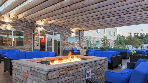 An outdoor seating area with stone fire pit, blue cushioned chairs, and a covered wooden pergola. - Fairfield Inn & Suites by Marriott Alexandria (Alexandria)