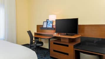 Una habitación de hotel con cama, escritorio con televisor, silla y un cubo de basura.