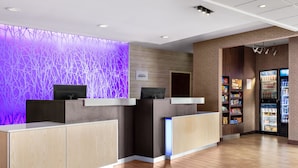 A reception area with a modern design, featuring a purple wall with a tree-like pattern, a wooden reception desk, and a refrigerator stocked with beverages. - Fairfield Inn & Suites by Marriott Alexandria (Alexandria)