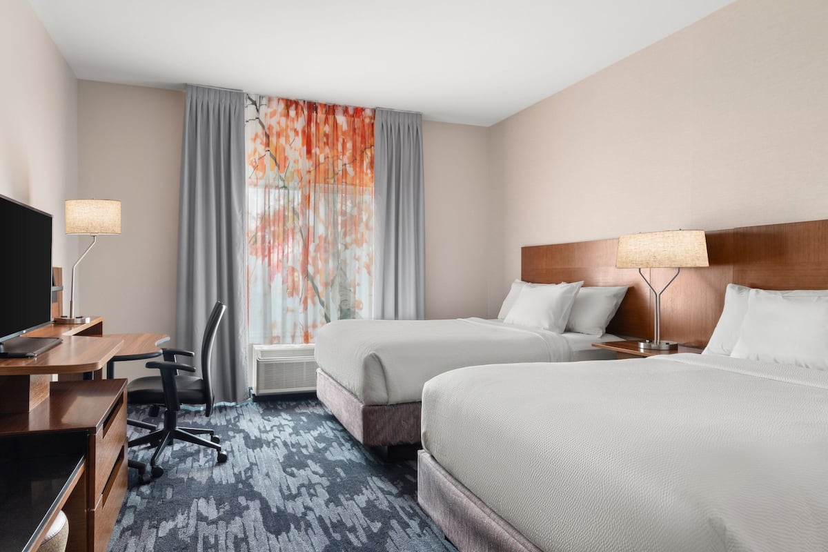 A hotel room with two beds, a desk with a computer, a chair, and a TV.