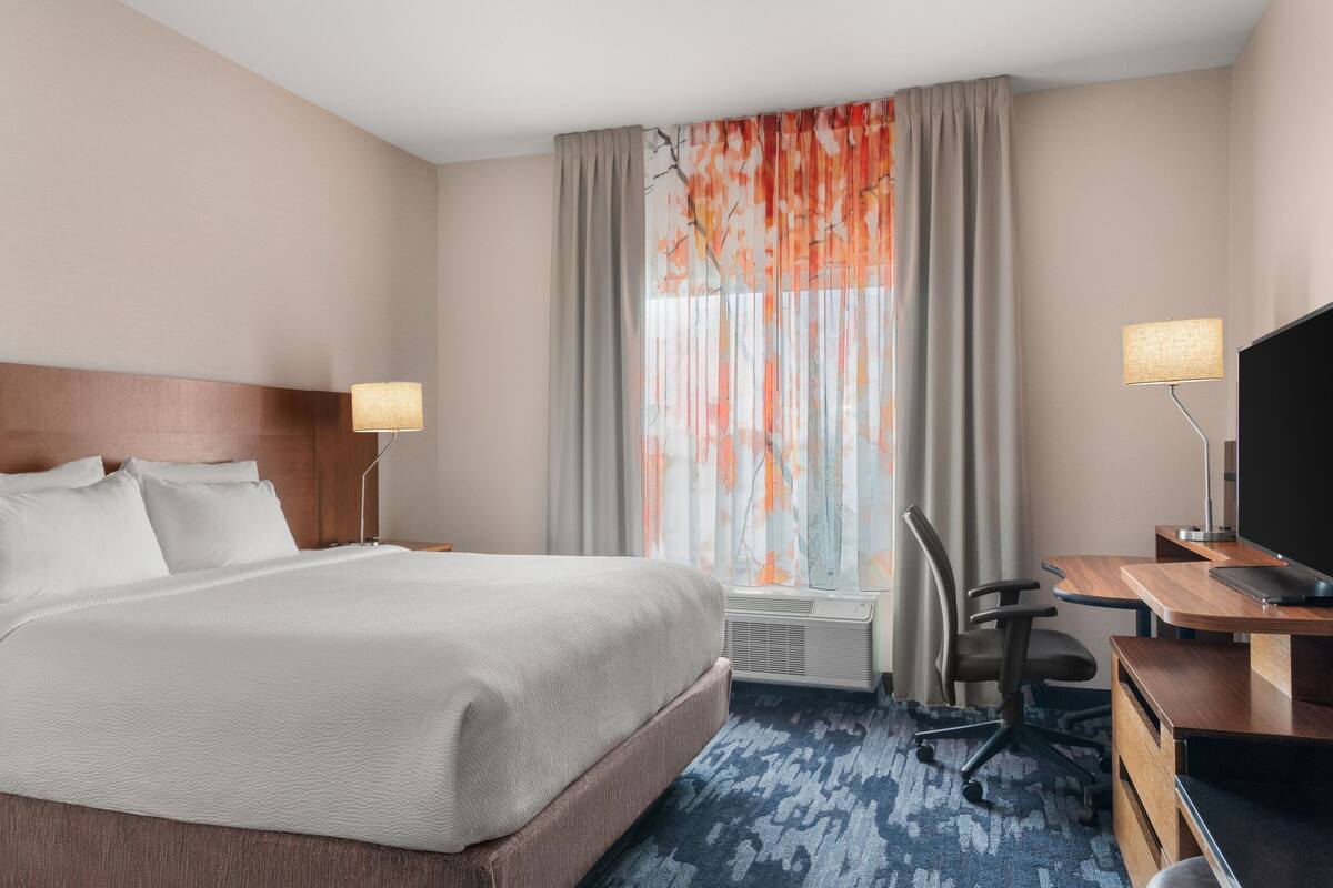 A hotel room with a large bed, a desk with a computer, a chair, and a TV.