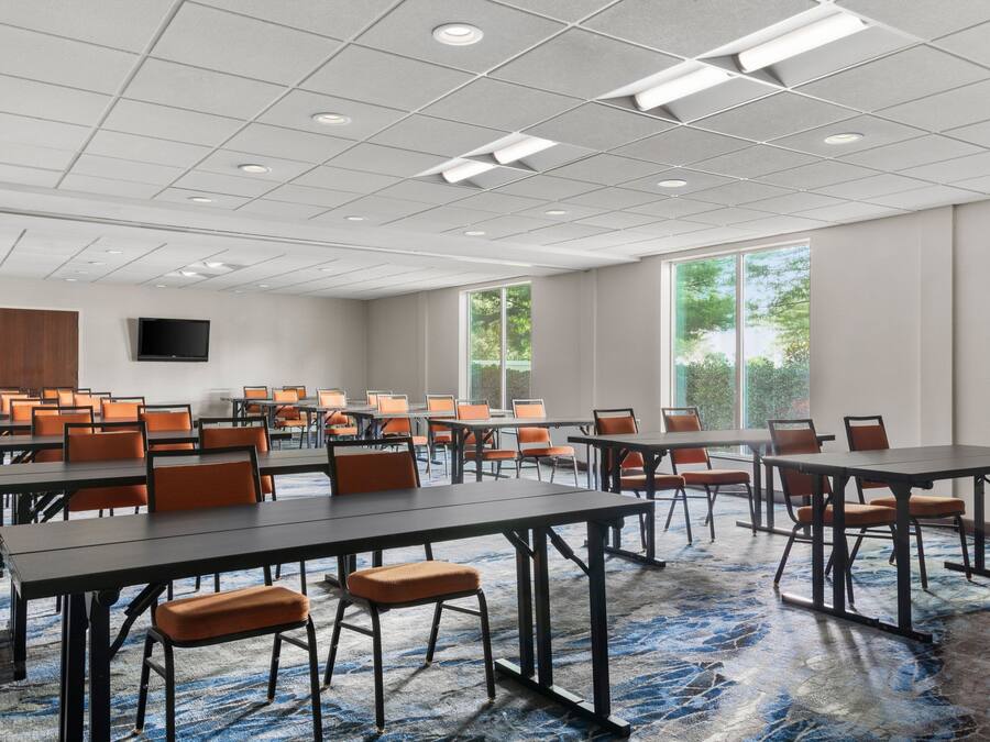 A conference room with multiple tables and chairs, large windows, and a flat-screen TV on the wall.