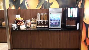 Eine Kaffeestation mit einer Kaffeemaschine, einem Getränkespender und einer Obstauslage.