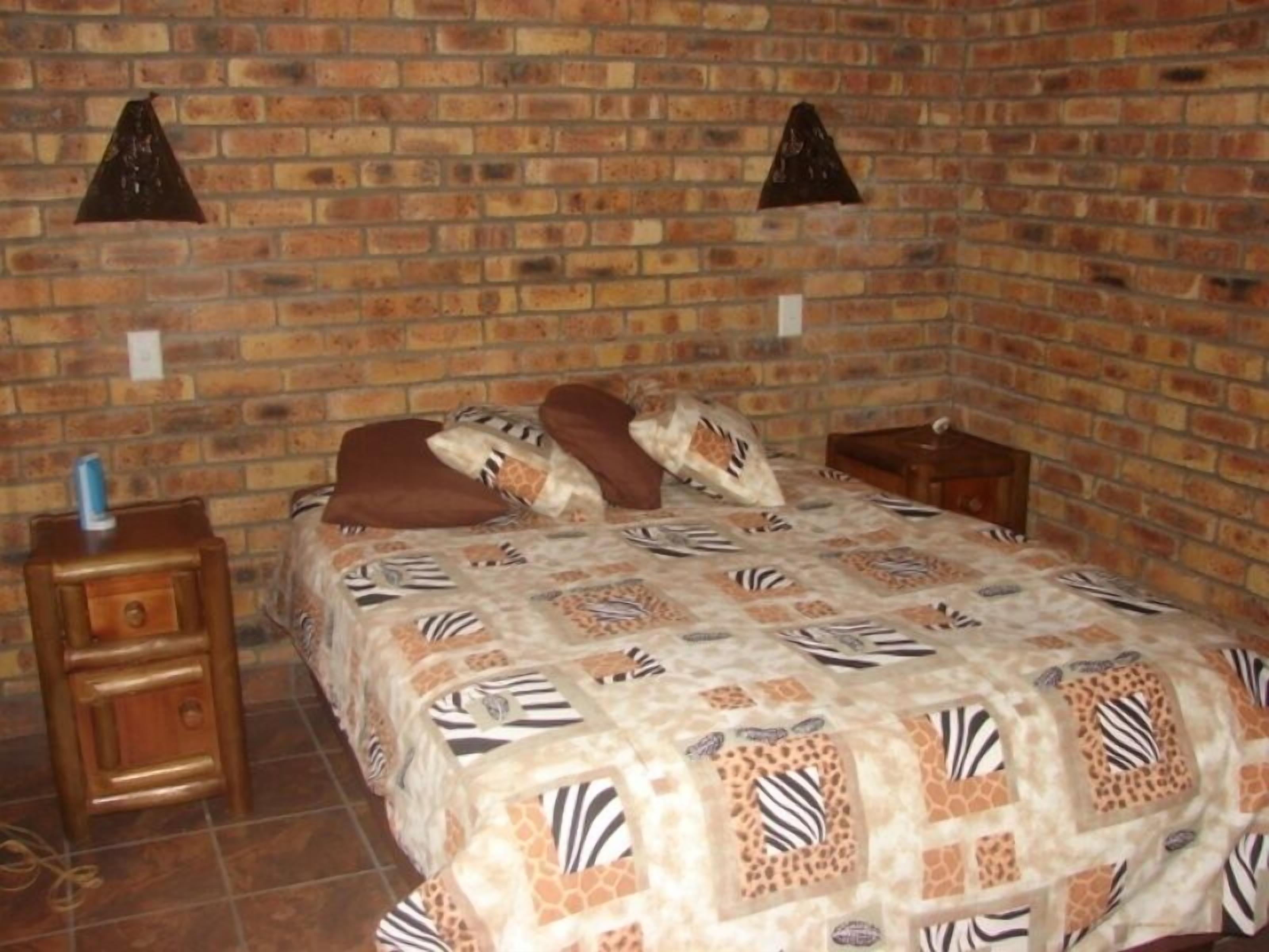 A room with a brick wall, a bed with a zebra-patterned bedspread, two nightstands, and a small table with a bottle on one of the nightstands.