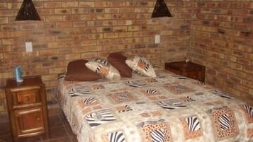 A room with a brick wall, a bed with a zebra-patterned bedspread, two nightstands, and a small table with a bottle on one of the nightstands.