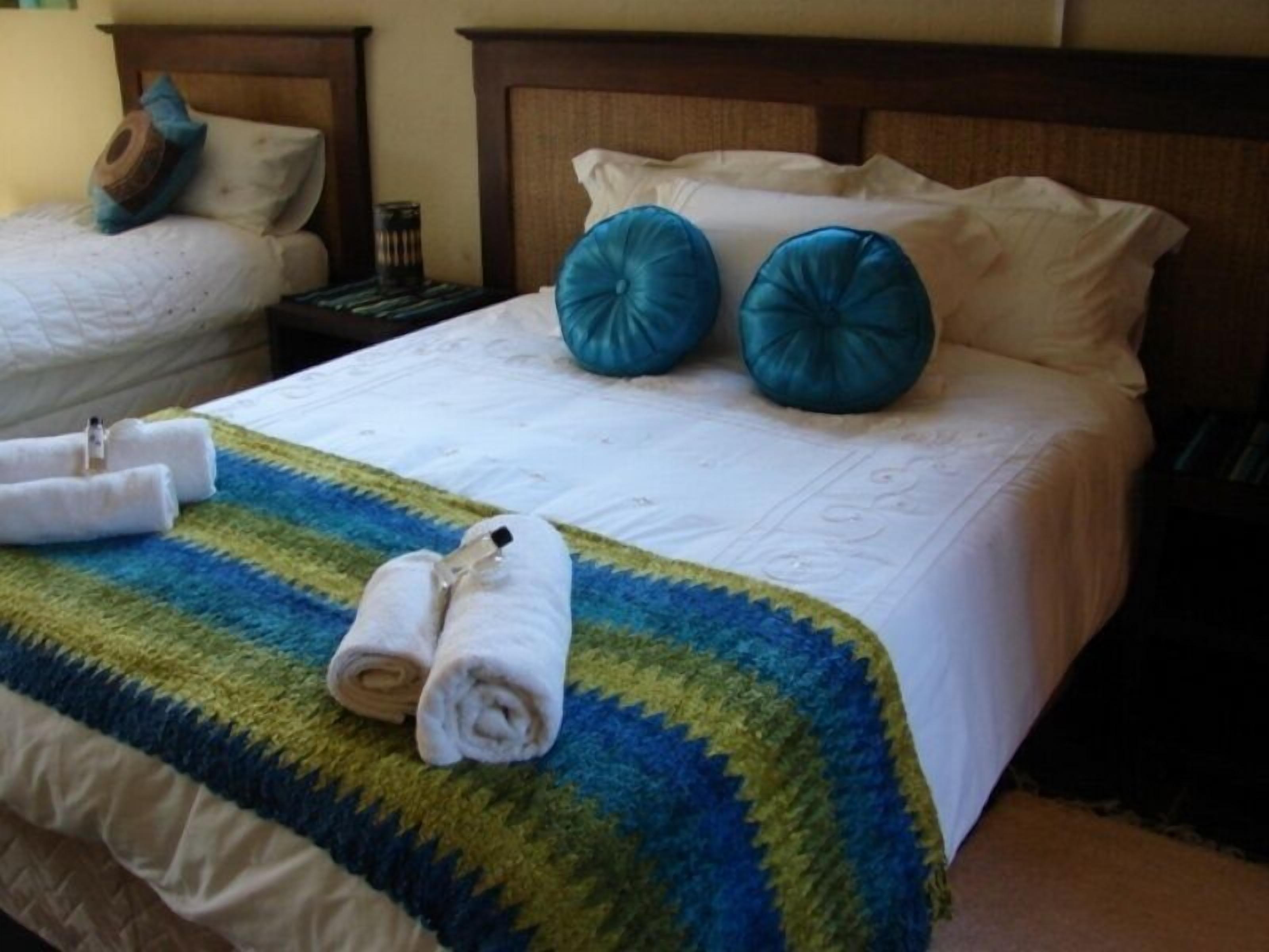 A hotel room with a neatly made bed, a blue and green striped blanket, and two rolled towels on the bed.