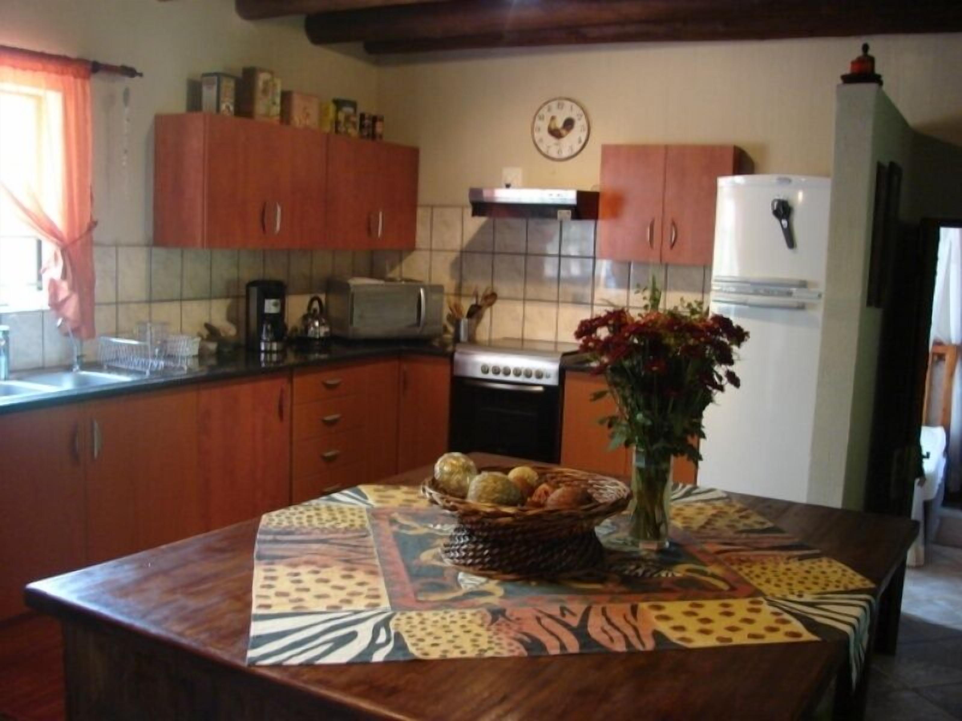 A kitchen with wooden cabinets, a stove, a refrigerator, and a table with a patterned tablecloth and a vase of flowers.