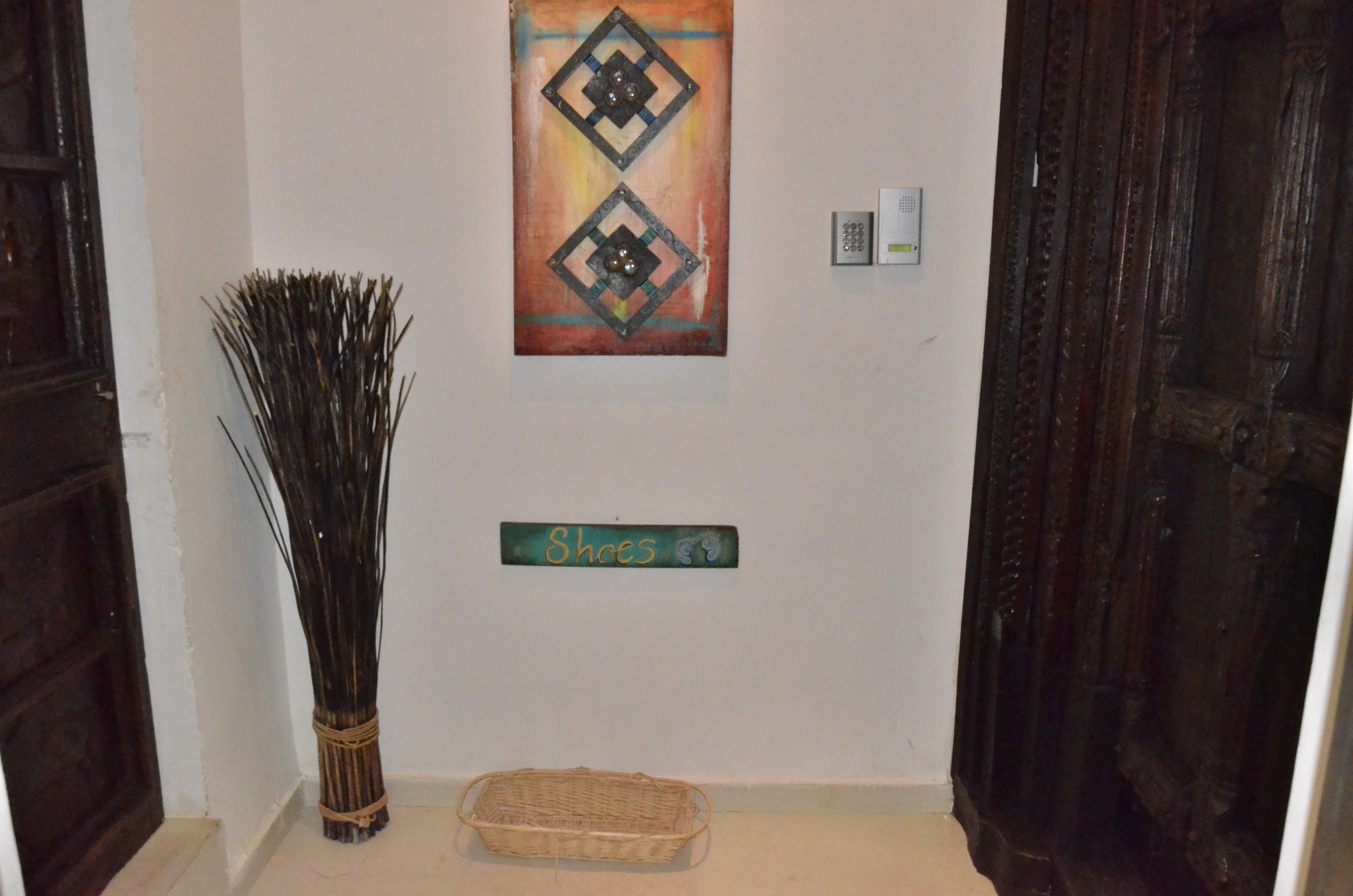 A hallway with a decorative painting, a sign labeled "Shoes", a wall-mounted intercom, and a wicker basket.