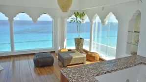 A room with a large window overlooking the sea, a bathtub, and a potted plant.