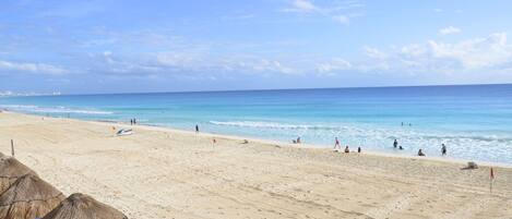 A beach with clear skies, a sandy shore, and a few people enjoying the water.