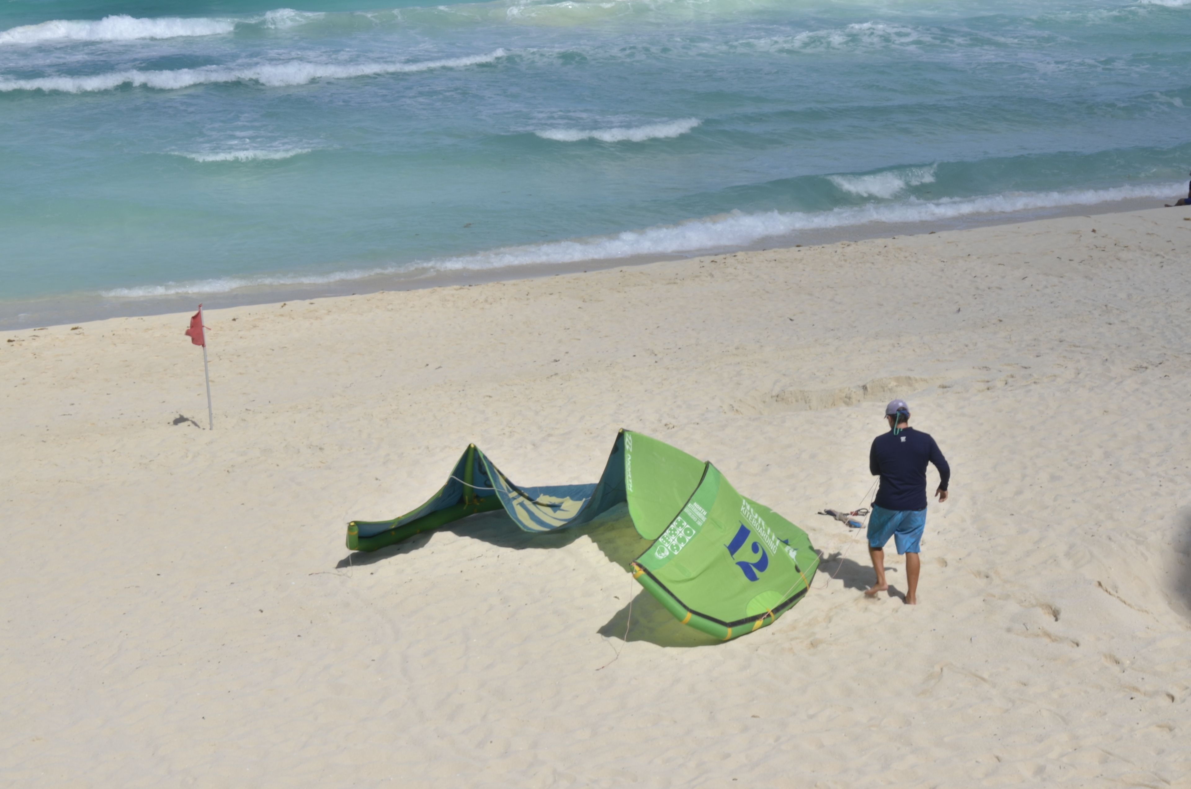 Una playa con una cometa verde y una bandera roja en la arena.
