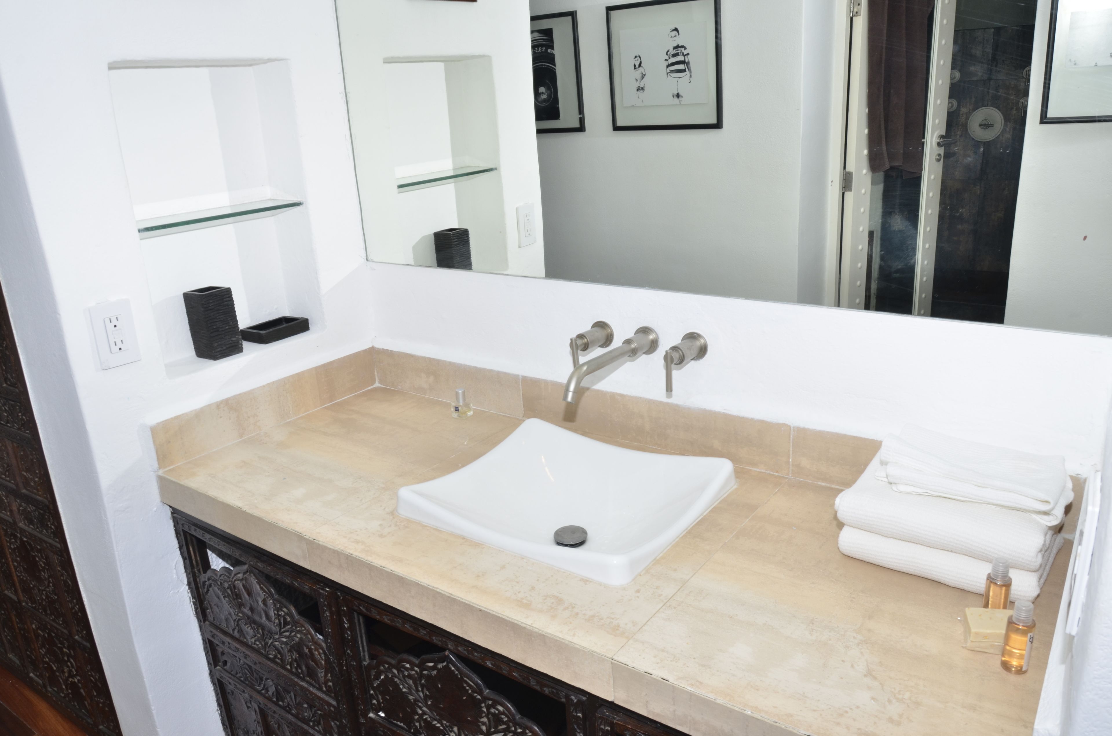 Une salle de bain avec un lavabo blanc, un comptoir beige et un miroir au-dessus. Des tableaux encadrés ornent le mur, et un porte-serviettes contient des serviettes.