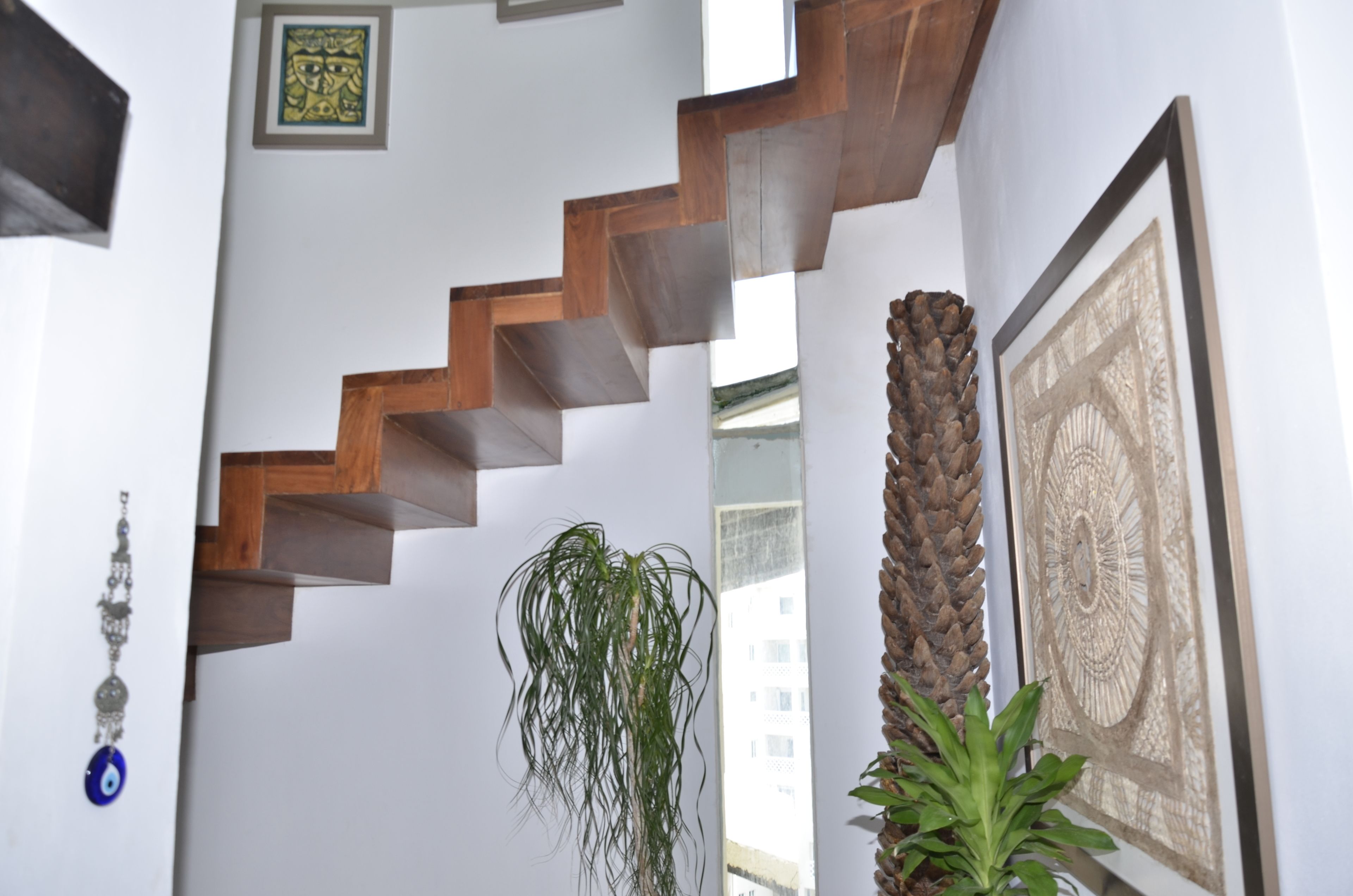 Una escalera con escalones de madera que ascienden, una planta colgante y una obra de arte enmarcada en la pared.