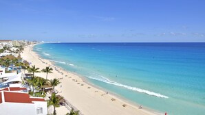 A beach with clear blue water, sandy shore, and palm trees.