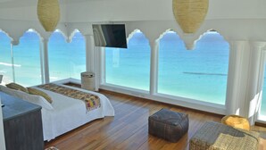 A room with a bed, a TV, and large windows with a view of the ocean.